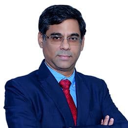 A professional man in a blue suit, red tie, and glasses looks forward.